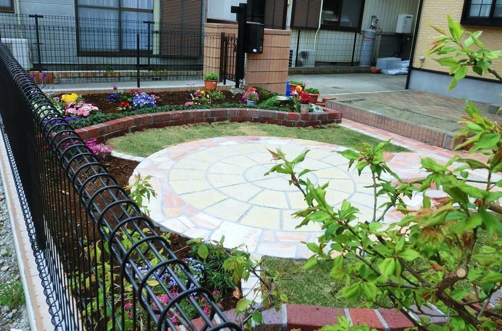 円形の石張りテラスとレンガ縁の花壇のある庭